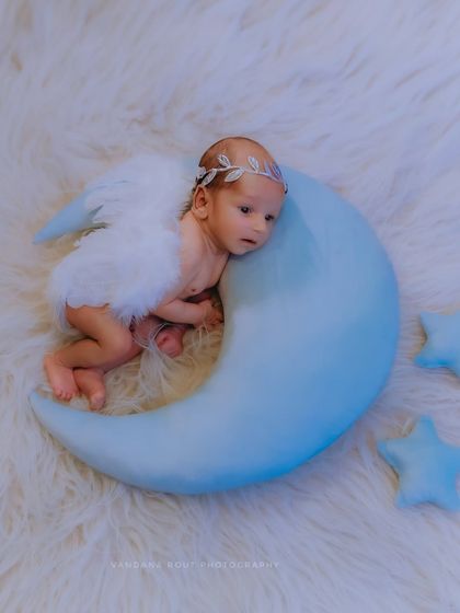 This image captures the newborn looking up, as if dreaming of the stars. The angel wings and moon prop create a magical setting for a truly special newborn photoshoot.