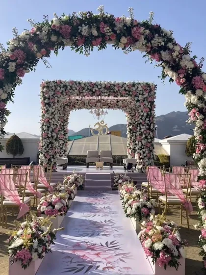 A grand floral entrance and aisle for a day wedding. The arches are covered in pink and white flowers, creating a fairytale-like pathway to the mandap.