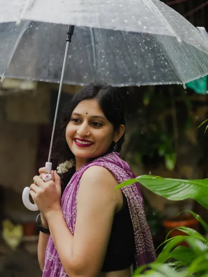 A sweet and gentle portrait taken during a rainy day shoot. The model peeks out from behind a large leaf while holding an umbrella, creating a playful and charming image.