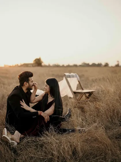 A wide shot of the couple enjoying a quiet moment in the vast open field. The simple setup with the chair adds a touch of elegance to the rustic, natural setting.