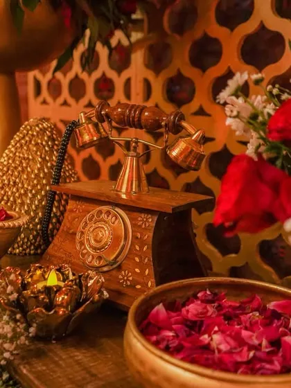 A nostalgic corner featuring a vintage rotary telephone, brass bowls with rose petals, and diyas, all set against a golden jali backdrop to evoke timeless charm.