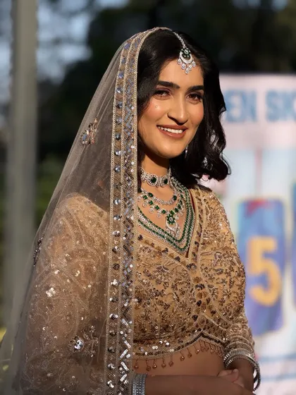 A close-up of the bride's happy face. The simple, elegant hairstyle with a sheer dupatta creates a timeless and sophisticated look.