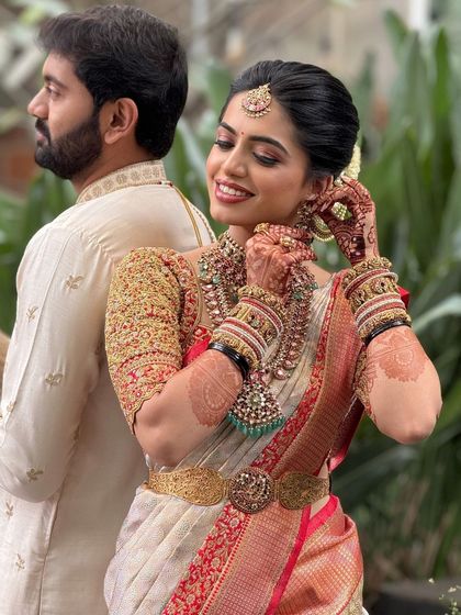 A beautiful candid moment of the bride adjusting her earring, with the groom in the background. The makeup is soft and romantic.