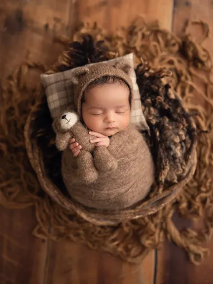 So cozy and cute. This newborn is swaddled in brown wool with a matching teddy bear hat and a tiny stuffed friend, perfect for a rustic-themed baby boy photoshoot.
