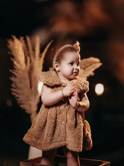 A stylish toddler in a cozy brown teddy bear dress. This nighttime outdoor shot with warm lighting creates a magical and fashionable portrait.