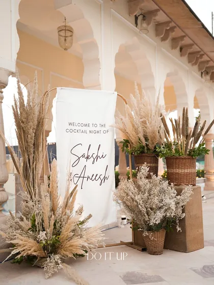 The welcome area for the bohemian cocktail night in Jaipur. A simple white banner is framed by large arrangements of pampas grass and other dried botanicals, setting a natural and chic tone.