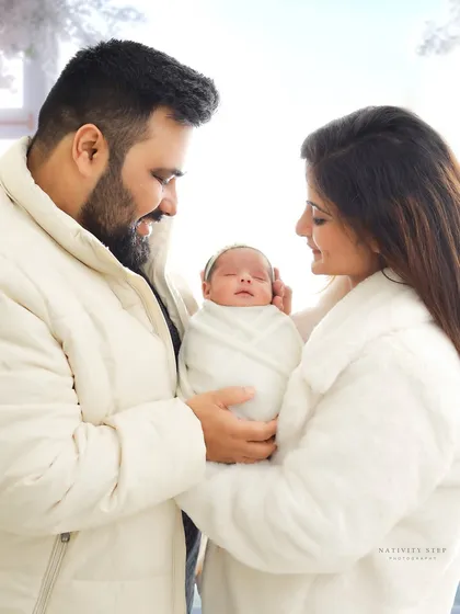 A heartwarming photo of both parents in cozy white jackets, lovingly holding their swaddled baby. This portrait perfectly captures the warmth and protection of a new family.
