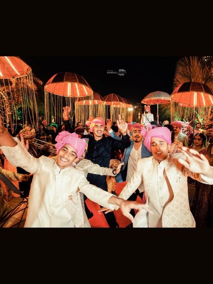The groom's squad making a high-energy entrance at the baraat. The vibrant pink turbans and joyful expressions capture the festive spirit of the celebration.