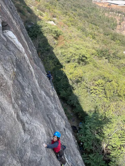 A climber smiles for the camera while on the wall at Varlakonda, with a stunning view of the valley below.