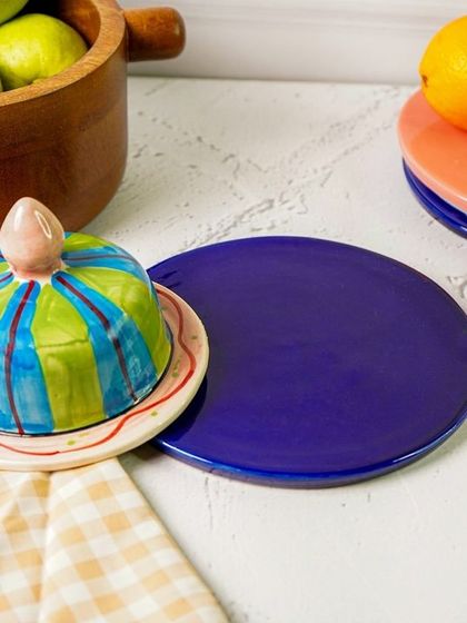 The butter dish styled with other colorful plates and a checkered napkin. This shot shows how the piece can be mixed and matched with other tableware.