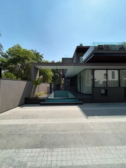 The contemporary form of Gulmohar Farmhouse, with its clean lines, glass walls, and a pool that is integrated into the main structure. The design creates a modern and sophisticated living experience.