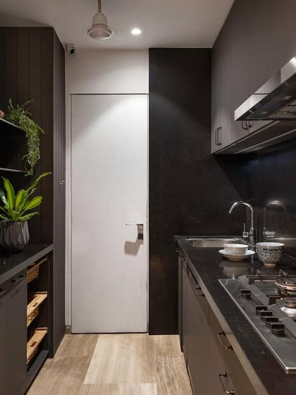 My happy place: the kitchen. This design uses dark, moody cabinetry and countertops, creating a sleek and sophisticated look. The open shelving with plants adds a touch of life and personality.