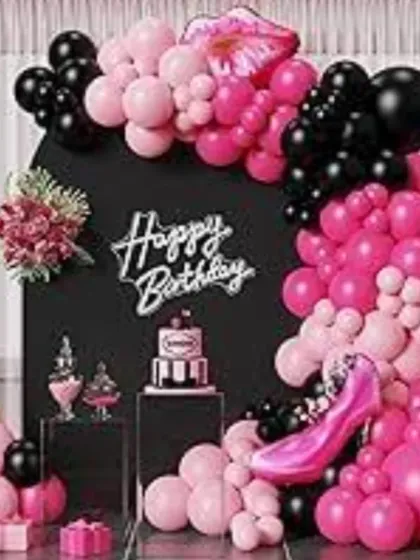A chic makeup-themed birthday party. The black backdrop is framed by a pink and black balloon arch, with foil balloons shaped like lipstick and high heels, and a dessert table with themed treats.