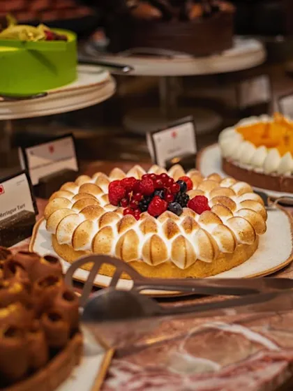 A beautiful lemon meringue tart displayed on a marble countertop among other desserts. The focus is on the perfectly toasted meringue peaks and fresh berry topping, creating a look of bakery-quality indulgence.
