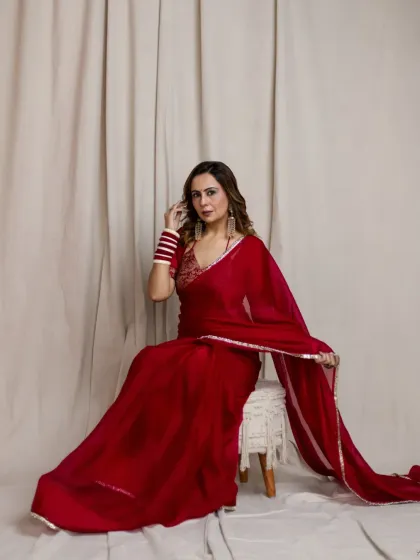 A confident and classic pose against a simple studio backdrop. The way the red saree drapes and falls is the centerpiece of this shot, showcasing its elegance and flow.