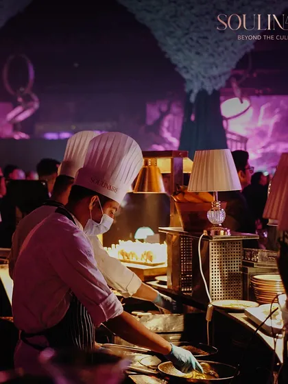 Our chefs working diligently at a busy live station, set against a backdrop of enchanting purple decor. We deliver excellence even in the most high-pressure environments.