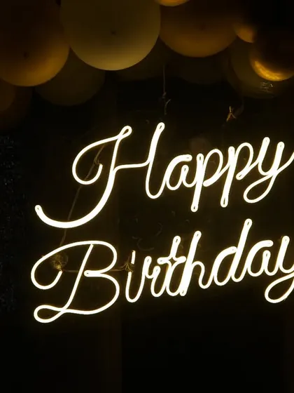A detailed shot of the "Happy Birthday" neon sign, a popular decoration for modern parties. We focus on capturing the mood and ambiance.