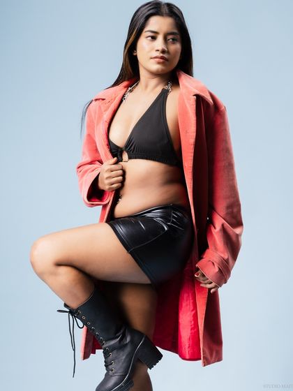 A model in a black bikini, leather skirt, and red coat, with a strong and confident pose.