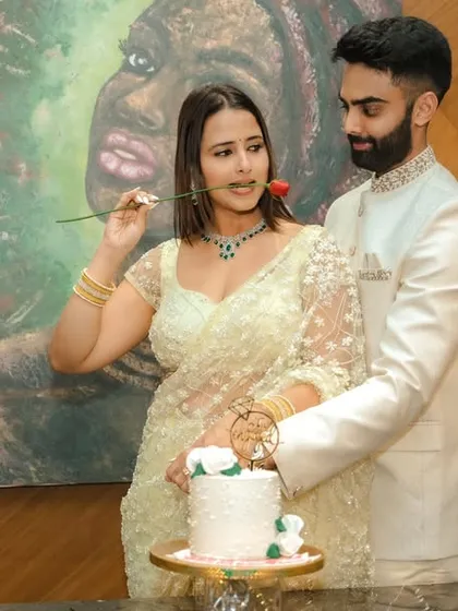 A joyous cake-cutting moment during an indoor engagement celebration in Pune. The couple's happiness is the focus, framed by modern decor and a beautiful piece of art, capturing the celebratory spirit of the occasion.