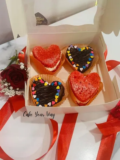 A box of four heart-shaped treats for your valentine. It includes two red velvet cream cheese sandwiches and two chocolate hearts with colorful sprinkles.