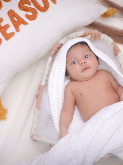 A newborn baby boy in a basket, with a "Snuggle Season" pillow nearby. We create cozy, themed setups that feel warm and personal.