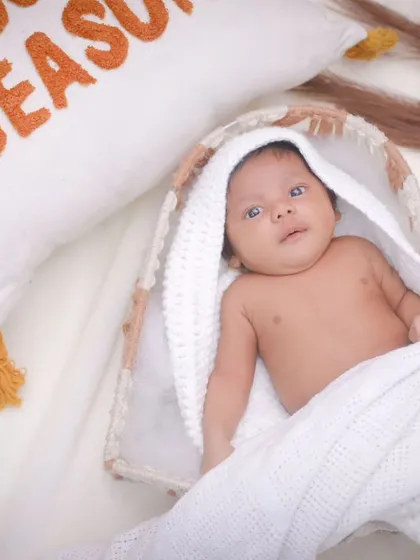A newborn baby boy in a basket, with a "Snuggle Season" pillow nearby. We create cozy, themed setups that feel warm and personal.