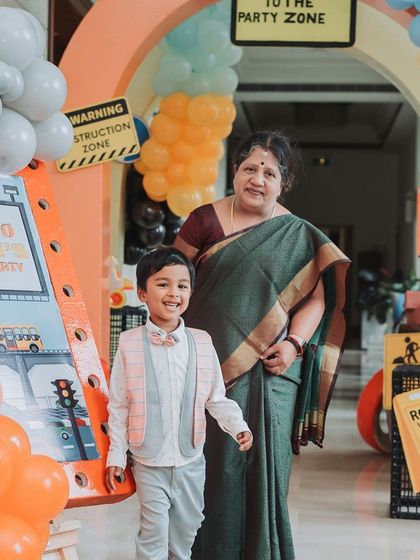 The birthday boy and his grandmother at the party entrance. The balloon arch and themed signs create a warm and festive welcome.