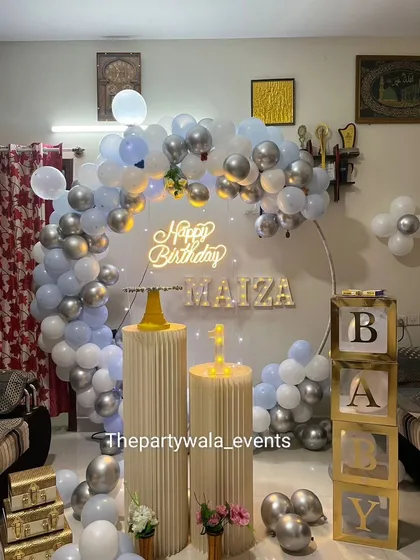 A beautiful ring decoration with silver, white, and light blue balloons. The "BABY" blocks and gold suitcases add a touch of vintage charm.