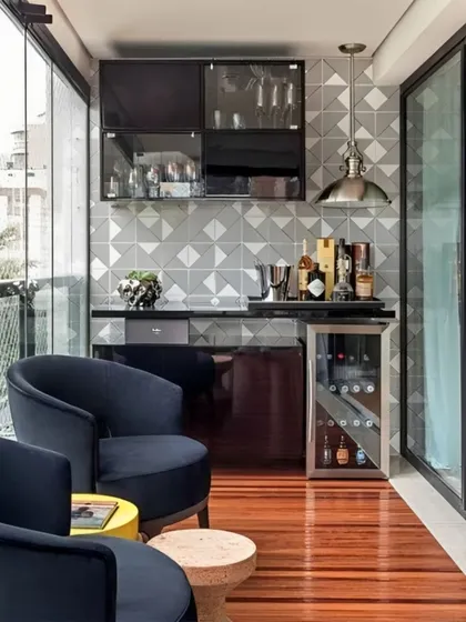 This sophisticated setup features a sleek, dark-toned bar with a dedicated wine cooler. The geometric tile backsplash and industrial-style pendant light add a modern, chic vibe, complemented by comfortable club chairs for a lounge-like feel.