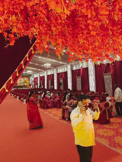 The atmosphere of a grand wedding hall, filled with vibrant red decor and floral arrangements hanging from the ceiling. We work with top decorators to bring your vision for a royal wedding to life.