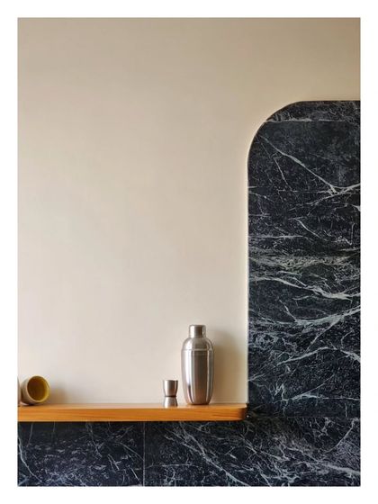 A minimalist bar nook where a simple wooden shelf is set against a dramatic arch of black marble. This composition is an exercise in restraint, allowing the beauty of the materials to speak for themselves.