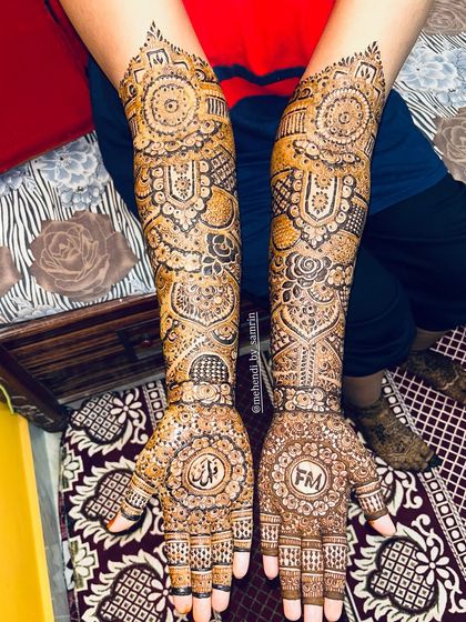 A beautiful bridal design that includes the initials "FM" and the groom's name in Arabic script on the palms.