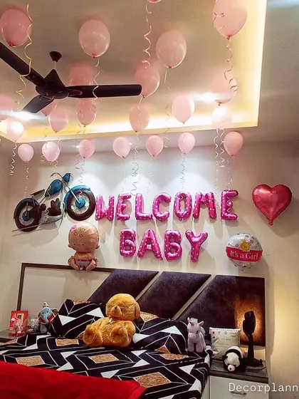 A lovely bedroom setup to welcome a baby girl. The pink "Welcome Baby" foil balloons are complemented by balloons floating on the ceiling, creating a dreamy and gentle atmosphere.