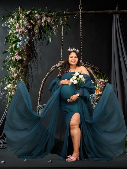 An elegant portrait of a woman on a floral swing, holding a bouquet of white flowers. Her regal pose and the beautiful studio setup create a timeless and graceful image.