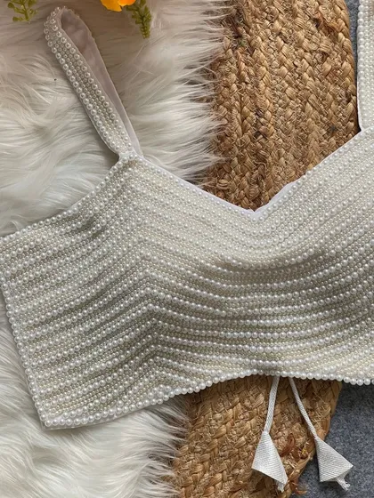 A close-up of my beautiful pearl moti spaghetti blouse in white. This trendy, padded blouse is handcrafted from pure silk and features heavy pearl work, making it a versatile and glamorous addition to your wardrobe.