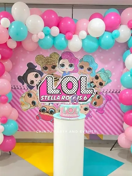 A LOL Surprise themed 6th birthday party. The decoration features a character backdrop framed by a pink, white, and teal balloon arch.