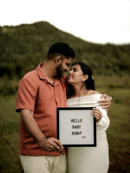 A classic couple portrait with an announcement sign. They hold a "Hello Baby Bump" letter board while sharing an intimate look, blending romance with the happy news.