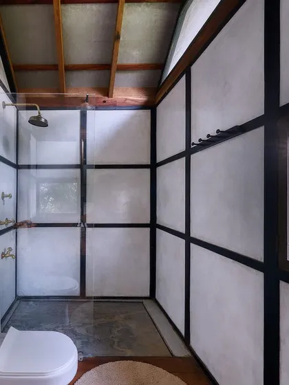 The shower area in the prefab cottage, where the walls are finished with a waterproof lime plaster that contrasts with the dark wood frame.