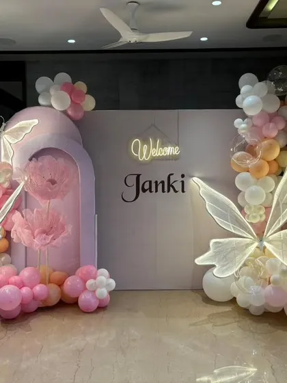 A close-up of the modern butterfly-themed welcome backdrop for baby Janki, showing the neon sign and lit-up wings.