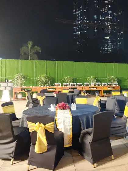 An outdoor reception setup at night. The tables are dressed in black and yellow, with the city skyline visible in the background, creating a chic and urban atmosphere for the celebration.