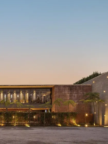 The exterior of Zero40 Brewery at sunset, showing the warm lighting on the brick facade and the surrounding landscape. The design creates a welcoming and atmospheric approach to the building.
