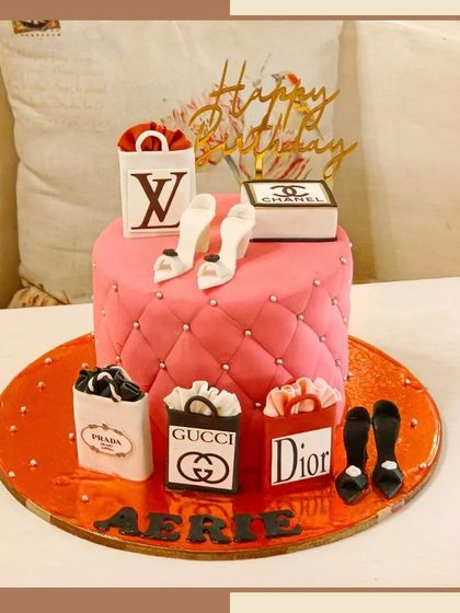 A high-fashion quilted pink cake adorned with edible shopping bags from Prada, Gucci, and Dior, and stylish high heels.