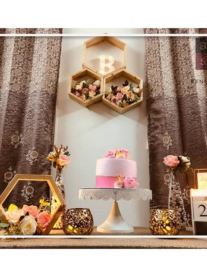 A closer look at the floral birthday decor. We used hexagonal wall shelves with a light-up initial 'B' and filled them with pink and white flowers to create a unique and personalized backdrop behind the cake table.