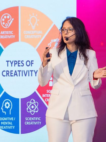 Speaking on stage in a white suit with a "Types of Creativity" slide. Every moment spent guiding my students and sharing my knowledge on stage fills my heart with purpose.