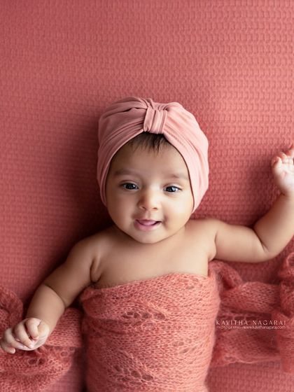Another angle of an older newborn, showing off their happy expression. The warm, peachy tones of the wrap and background create a joyful and inviting image.