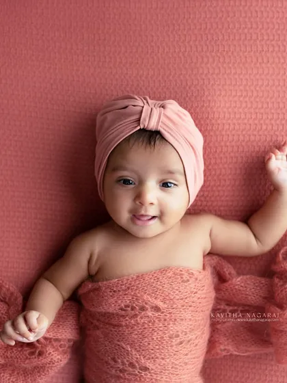 Another angle of an older newborn, showing off their happy expression. The warm, peachy tones of the wrap and background create a joyful and inviting image.