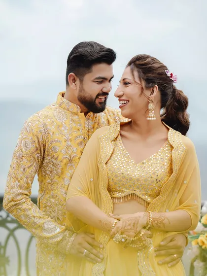 A happy, bright portrait of the couple in their coordinated yellow Haldi outfits, smiling at each other against a scenic mountain backdrop.