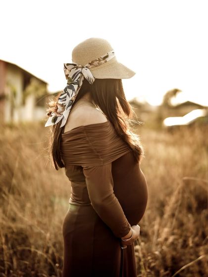 A stylish and anonymous portrait from behind, with the mom-to-be looking out over a golden field, her hat adding a touch of elegance.