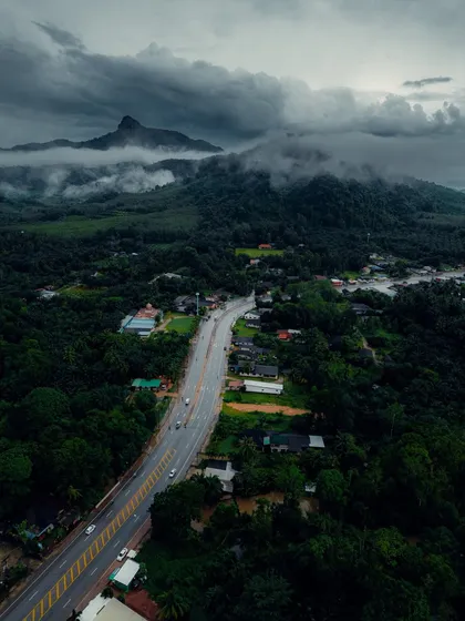 An aerial view of a highway cutting through the lush green landscape of Krabi, with dramatic mountains in the background.