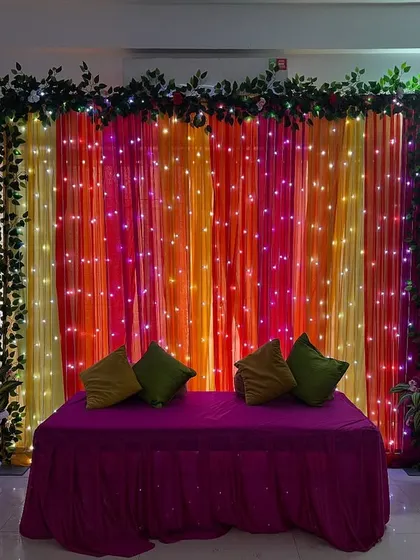 A simple and beautiful backdrop created with colorful drapes and fairy lights, perfect for home-based functions like Mehendi or a Chowki.